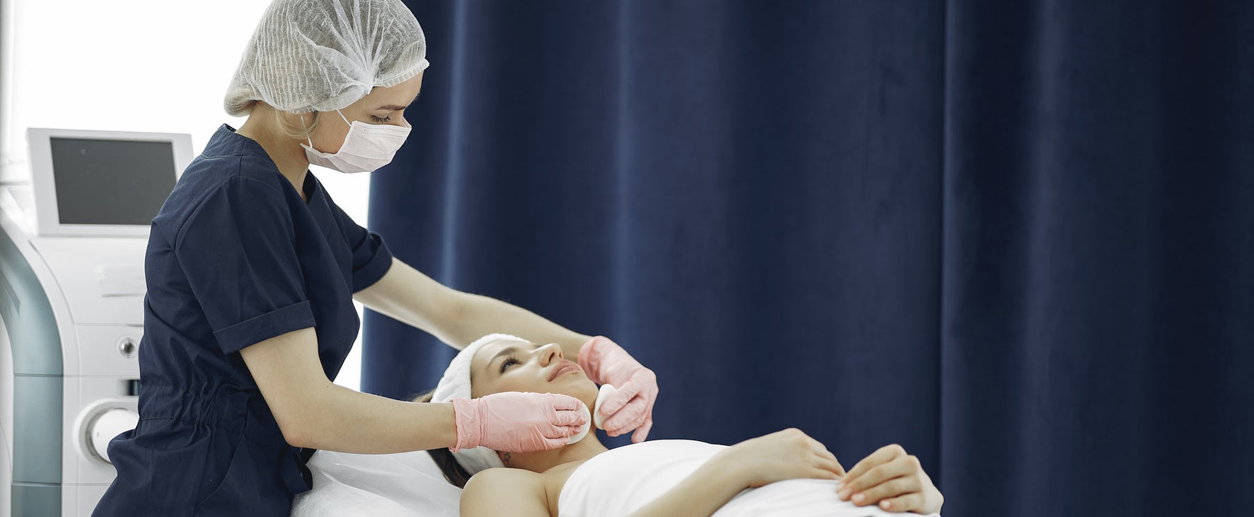 cosmetic nurse with mask performing facial treatment on female patient