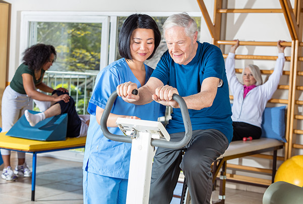 physical therapist assisting elderly patient on machine during rehab workout, while following best practices to mitigate malpractice risk